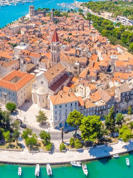 Aerial view of Trogir's historic center with red-roofed buildings and surrounding turquoise waters.
