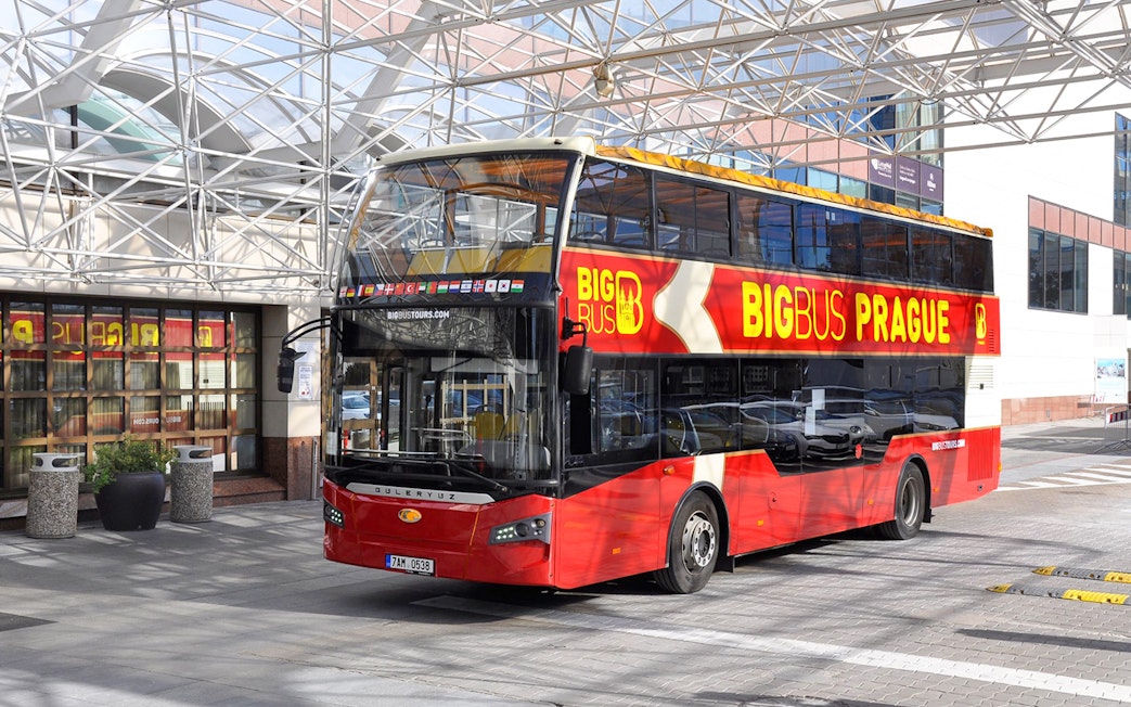 Red double-decker bus for Prague hop-on hop-off tour parked under a glass canopy.