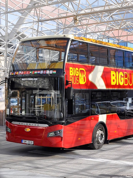 Red double-decker bus for Prague hop-on hop-off tour parked under a glass canopy.