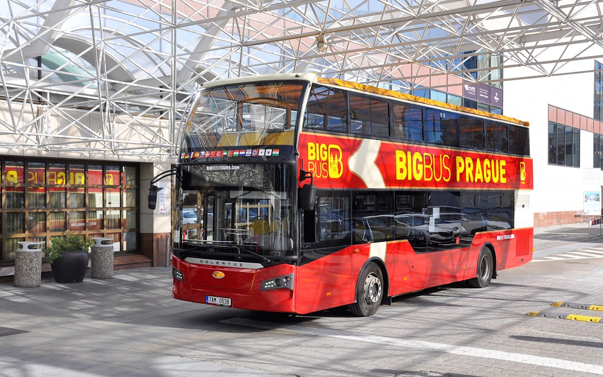 Red double-decker bus for Prague hop-on hop-off tour parked under a glass canopy.