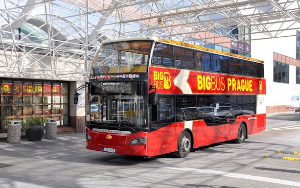 Red double-decker bus for Prague hop-on hop-off tour parked under a glass canopy.