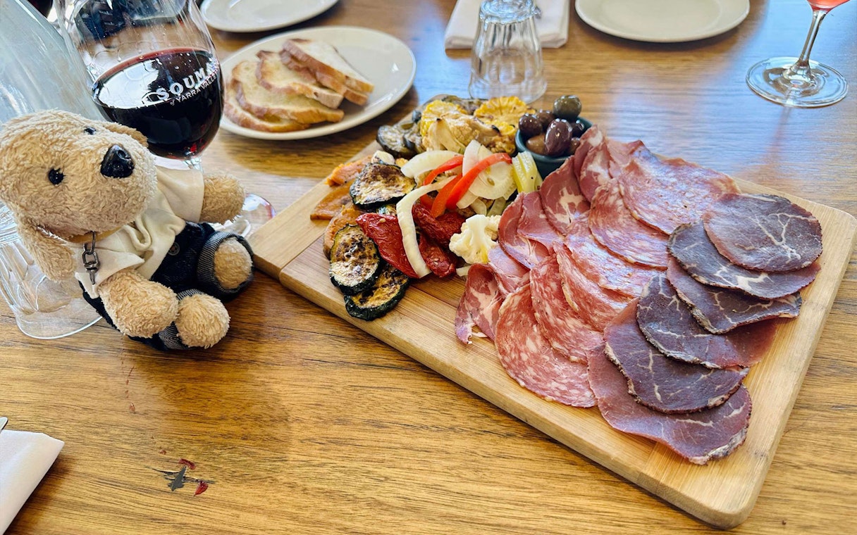 Charcuterie board with meats and vegetables, wine glass, and teddy bear on Yarra Valley tour.