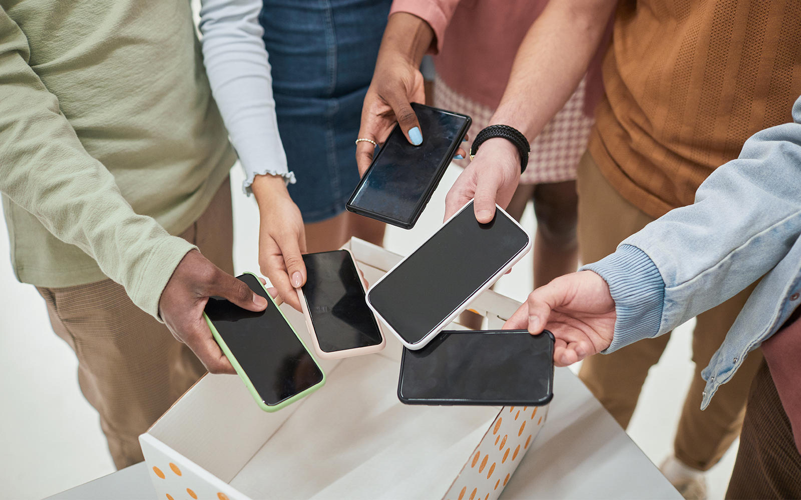 Top view closeup of diverse group of teenagers putting smartphones in box