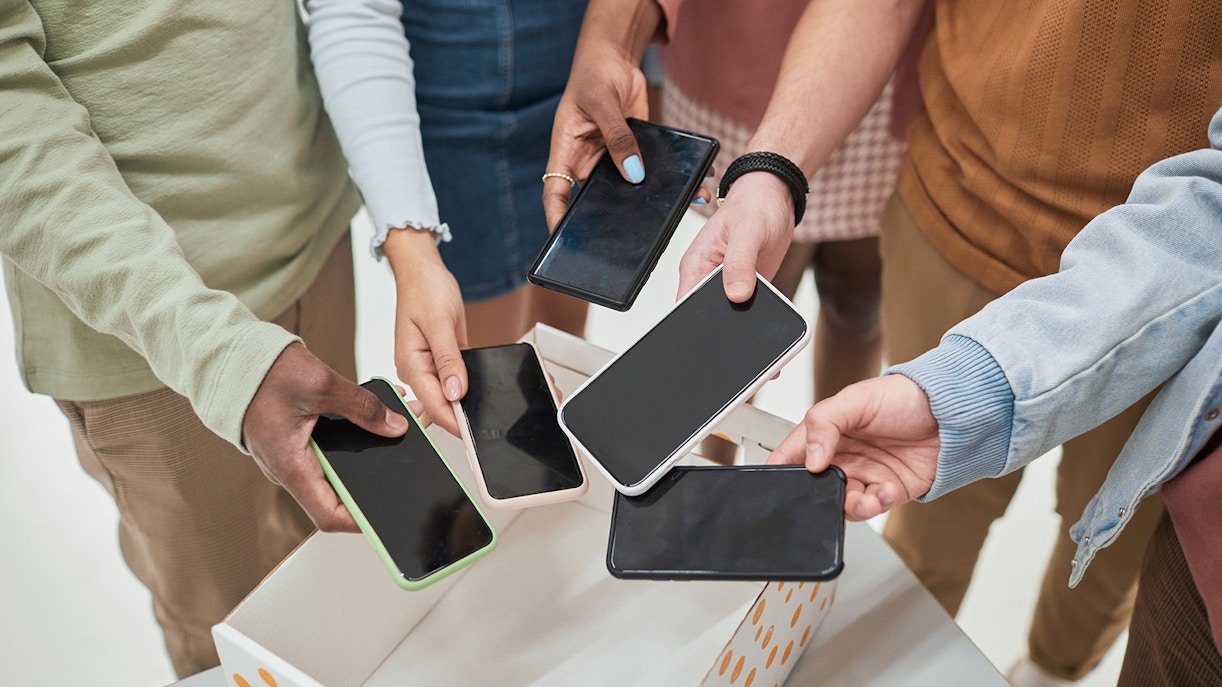 Top view closeup of diverse group of teenagers putting smartphones in box