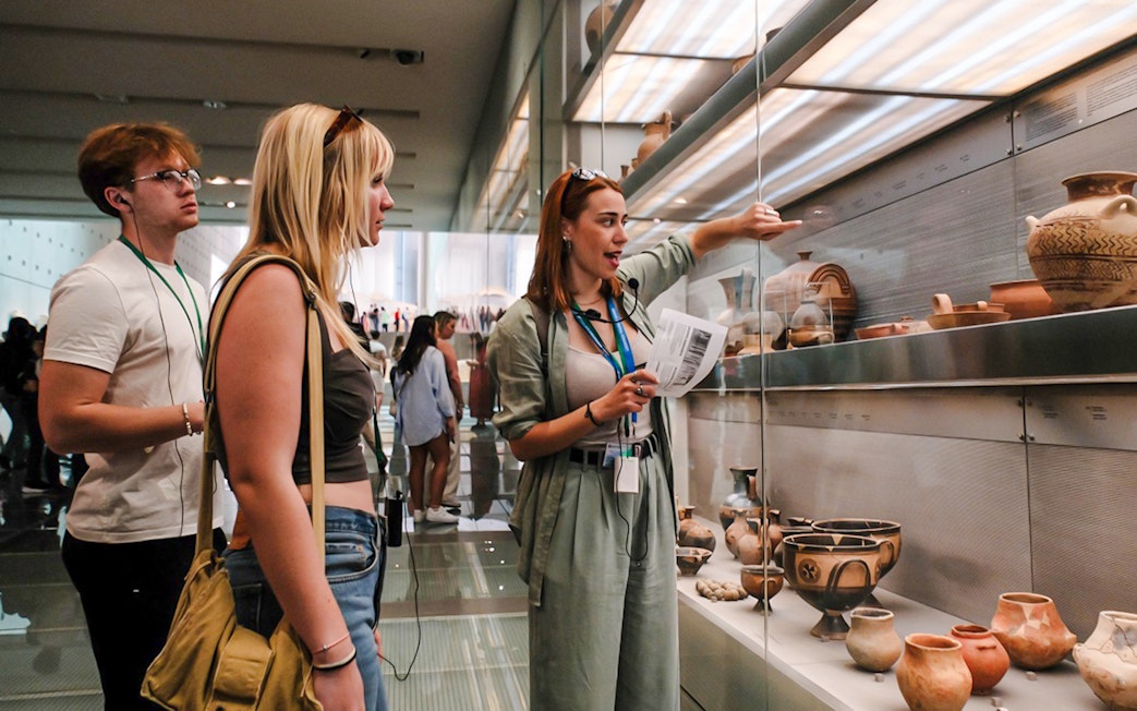 Visitors on a guided tour in Acropolis Museum viewing ancient pottery exhibits.