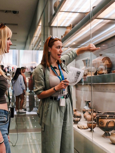 Visitors on a guided tour in Acropolis Museum viewing ancient pottery exhibits.