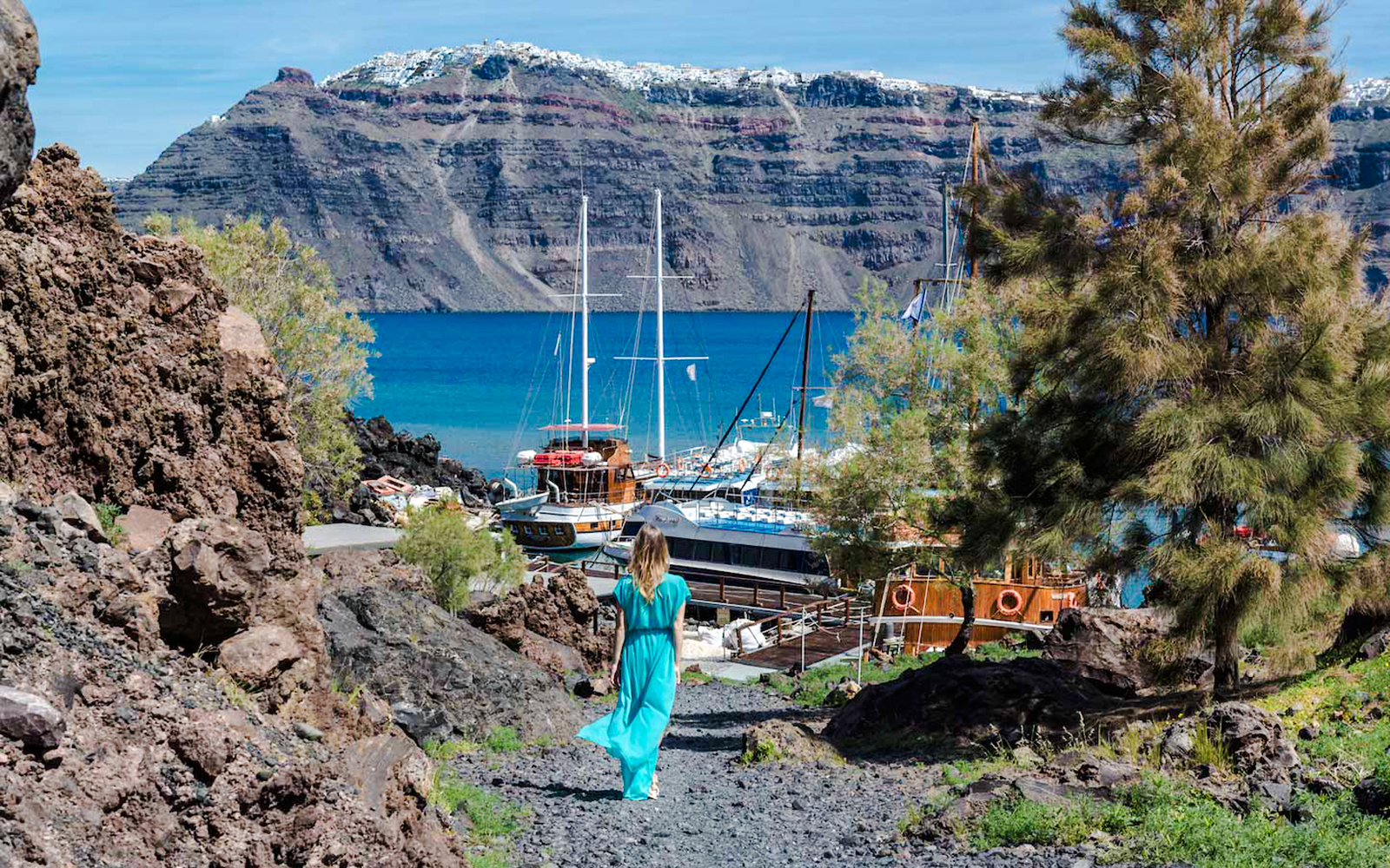 Guests walking on volcanic path towards boats in Santorini, Greece.
