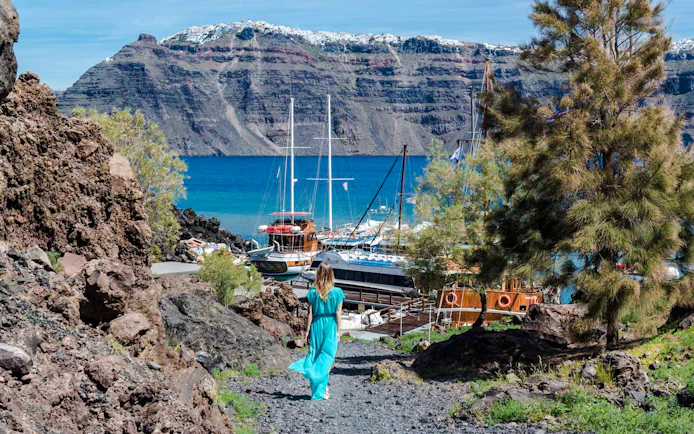 Guests walking on volcanic path towards boats in Santorini, Greece.