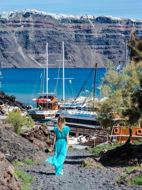 Guests walking on volcanic path towards boats in Santorini, Greece.