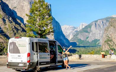 Tour van at Yosemite National Park viewpoint with Half Dome in background.