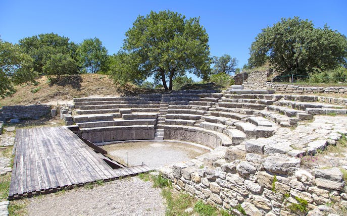 Ancient amphitheater ruins in Troy, Turkey, surrounded by trees under a clear sky.