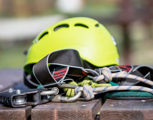Climbing helmet and gear on a wooden table, featuring ropes and carabiners.