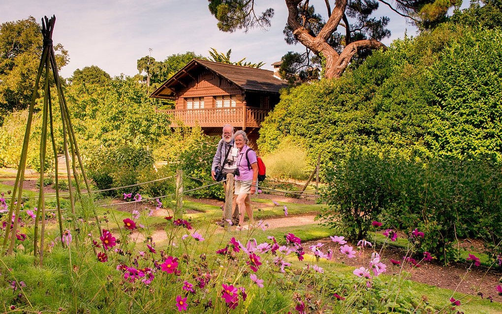 Couple walking in garden near Swiss-style cottage surrounded by lush greenery.