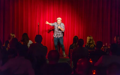 Comedian performing on stage at The Comedy Embassy with audience watching.