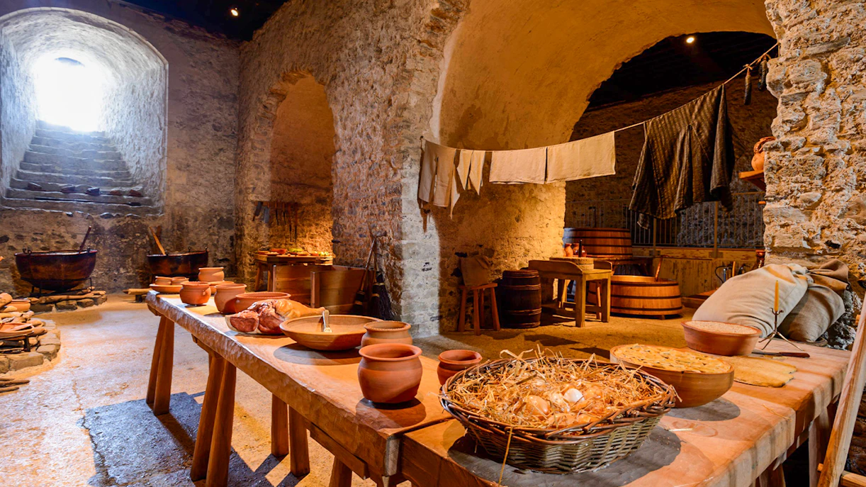 Dover Castle interior kitchen with stone walls, wooden tables, and medieval cooking utensils.