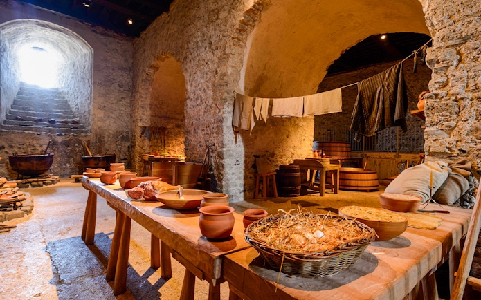Dover Castle interior kitchen with stone walls, wooden tables, and medieval cooking utensils.