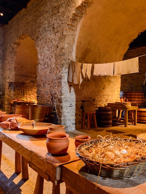 Dover Castle interior kitchen with stone walls, wooden tables, and medieval cooking utensils.