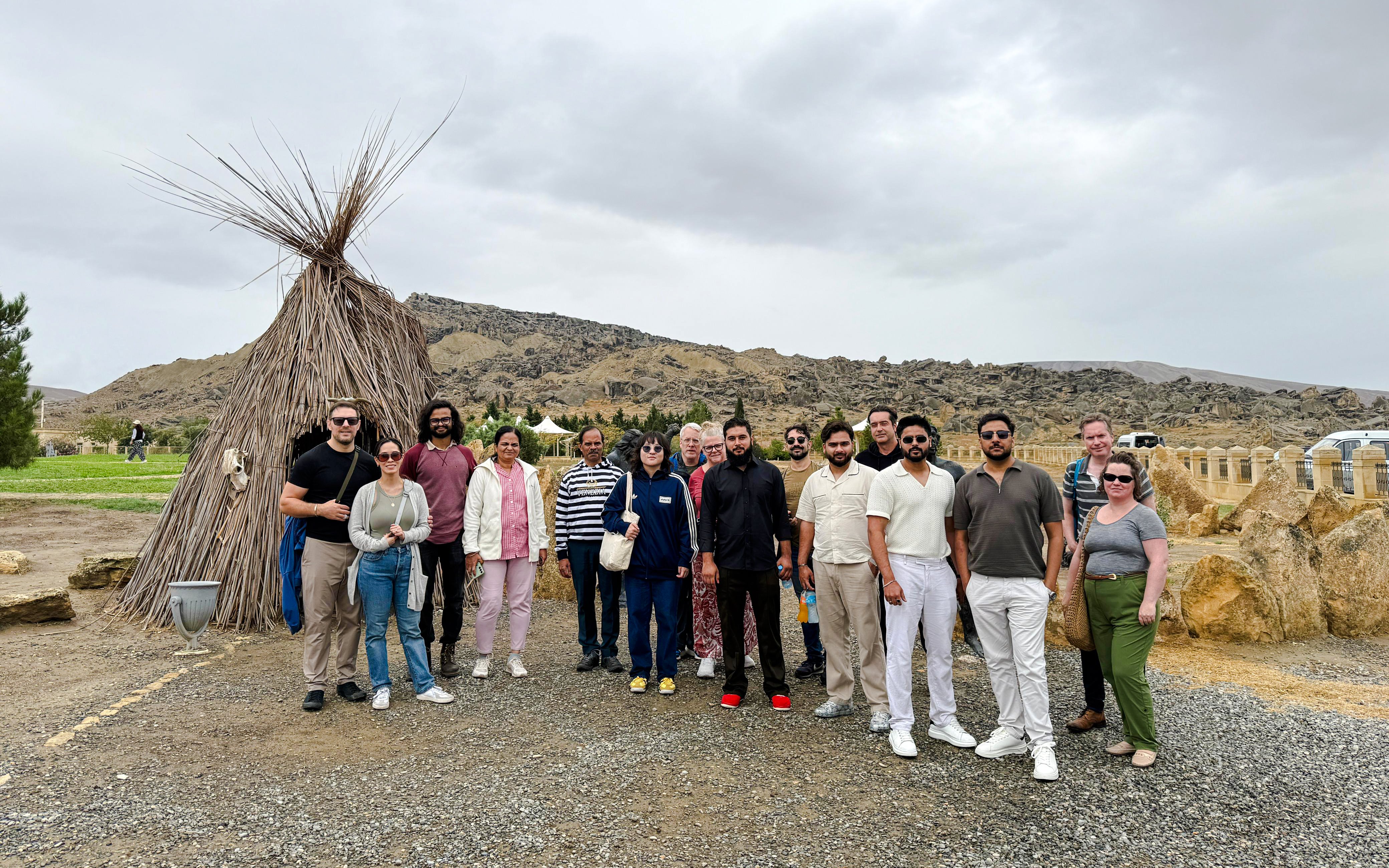 Group of tourists at Gobustan National Park with traditional hut and rocky landscape in the background.