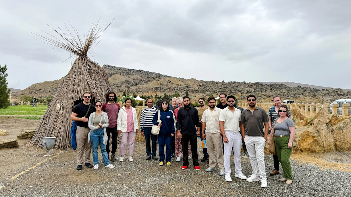 Group of tourists at Gobustan National Park with traditional hut and rocky landscape in the background.