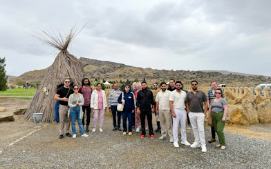 Group of tourists at Gobustan National Park with traditional hut and rocky landscape in the background.