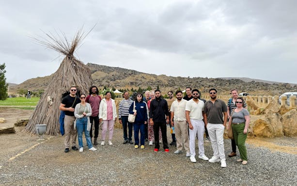 Group of tourists at Gobustan National Park with traditional hut and rocky landscape in the background.