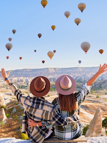 Couple watching hot air balloons over Cappadocia landscape, Turkey.
