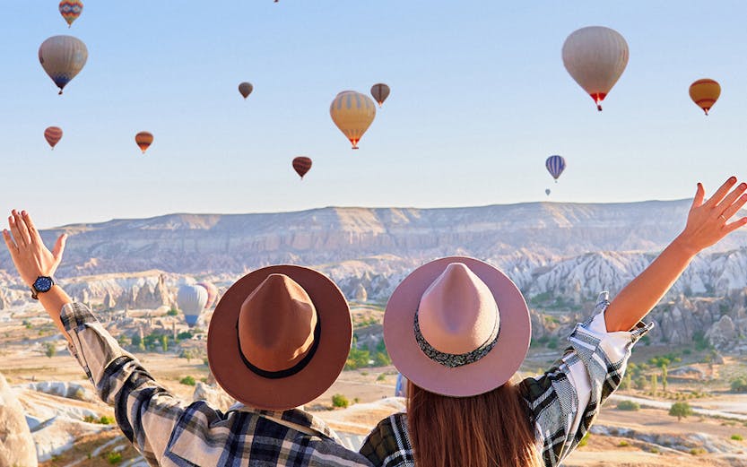 Couple watching hot air balloons over Cappadocia landscape, Turkey.