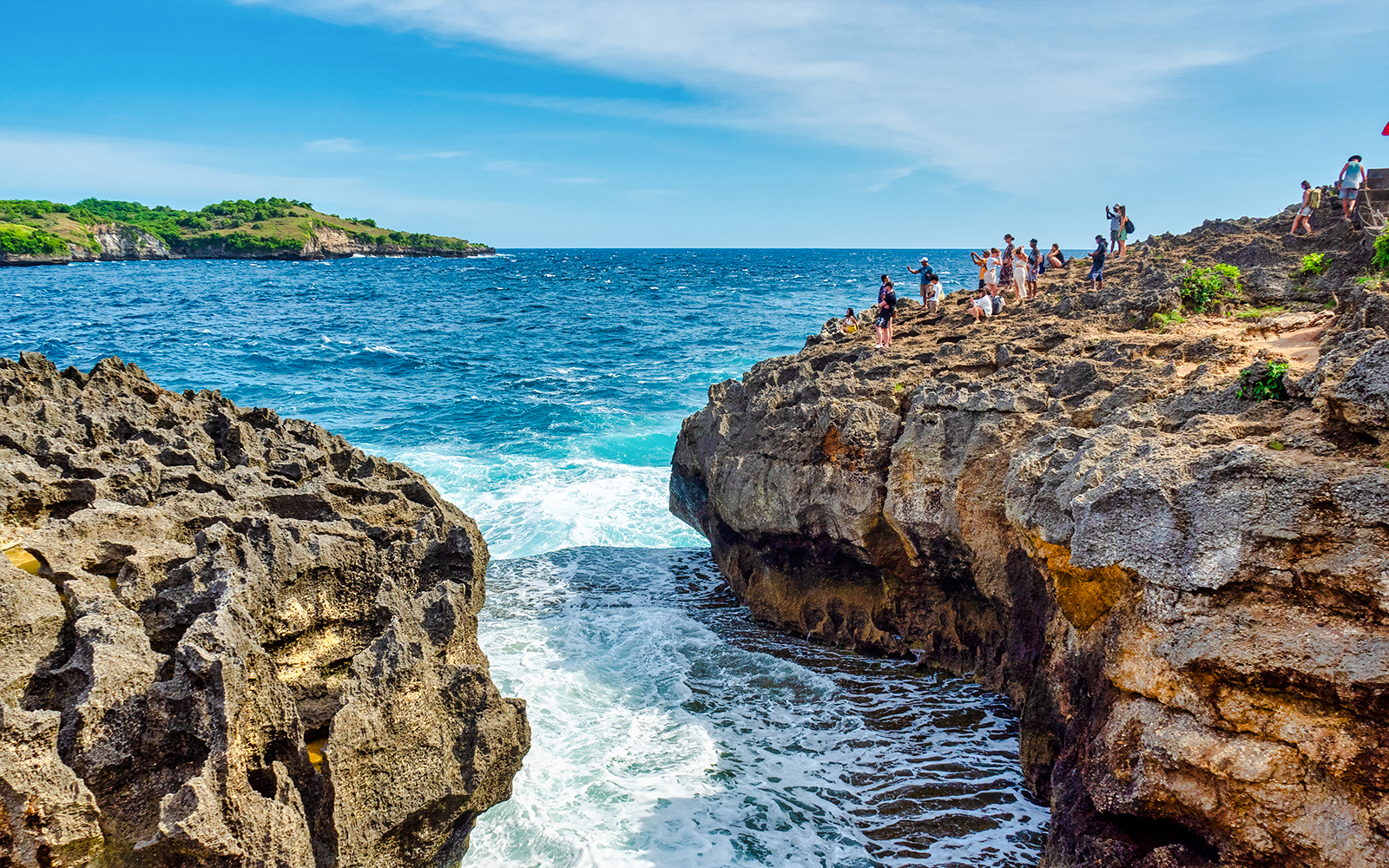 Visitors exploring rocky cliffs at Angel's Billabong, Nusa Penida with ocean waves below.