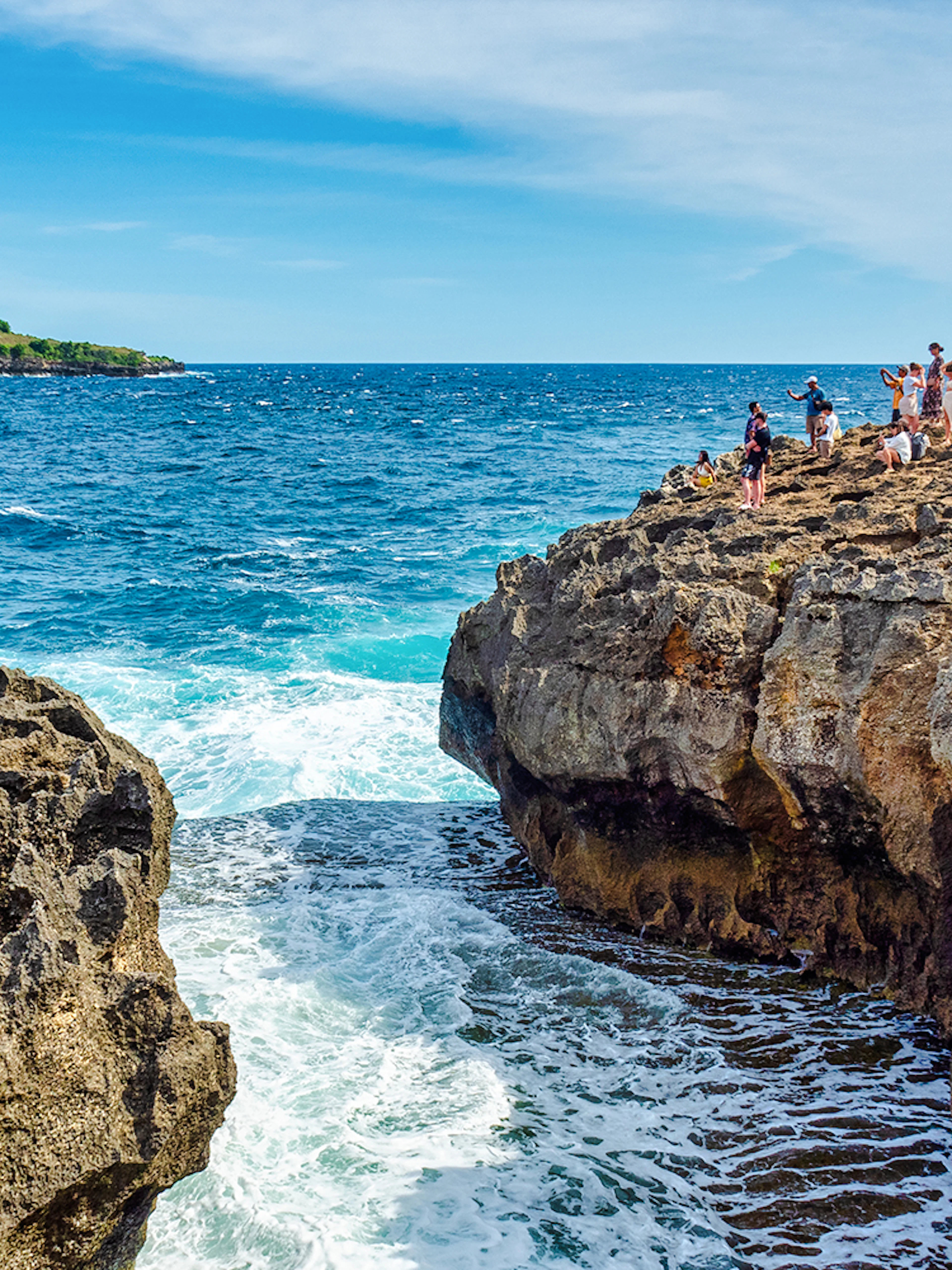 Visitors exploring rocky cliffs at Angel's Billabong, Nusa Penida with ocean waves below.