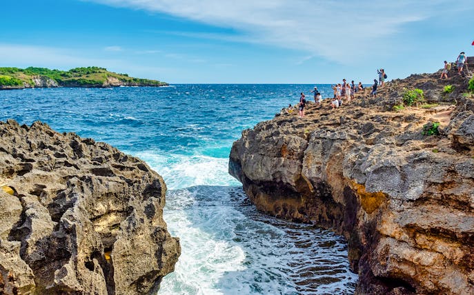 Visitors exploring rocky cliffs at Angel's Billabong, Nusa Penida with ocean waves below.