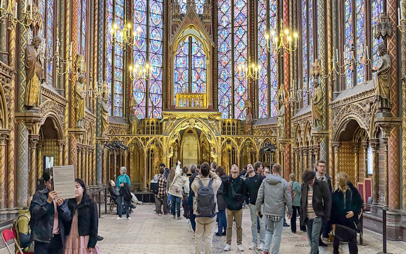 Visitors inside Sainte Chapelle, Paris, admiring stained glass windows and ornate Gothic architecture.