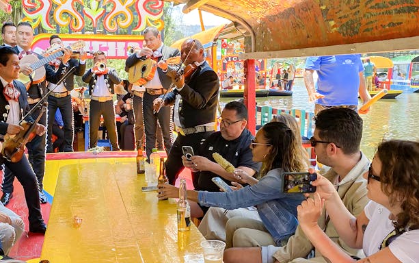 Guests enjoying mariachi band on Trajinera Party boat in Xochimilco, Mexico.