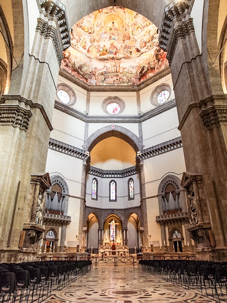 Florence Duomo interior with frescoed dome and rows of chairs.