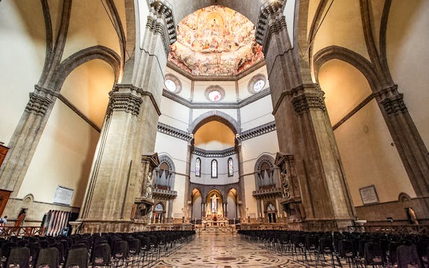 Florence Duomo interior with frescoed dome and rows of chairs.