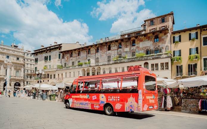 Red hop-on hop-off bus in Verona's historic Piazza delle Erbe, Italy.