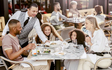 Family dining outdoors at American Dream with waiter serving food.