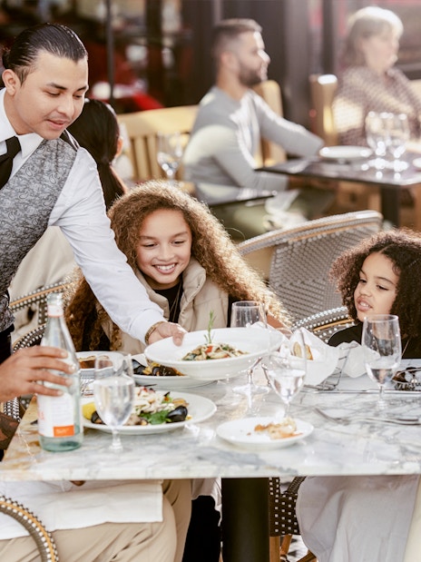 Family dining outdoors at American Dream with waiter serving food.