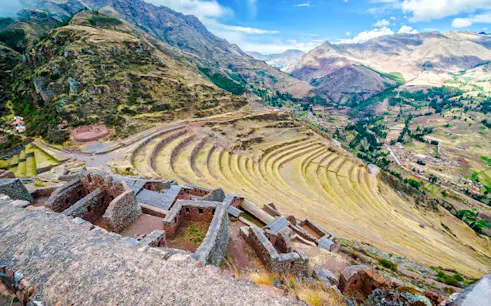 Terraced fields and ruins in Sacred Valley, Peru, with mountains in the background.