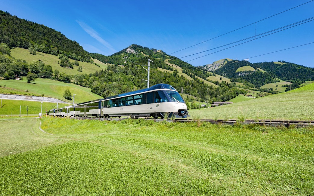 Train traveling through green hills and mountains in Switzerland.
