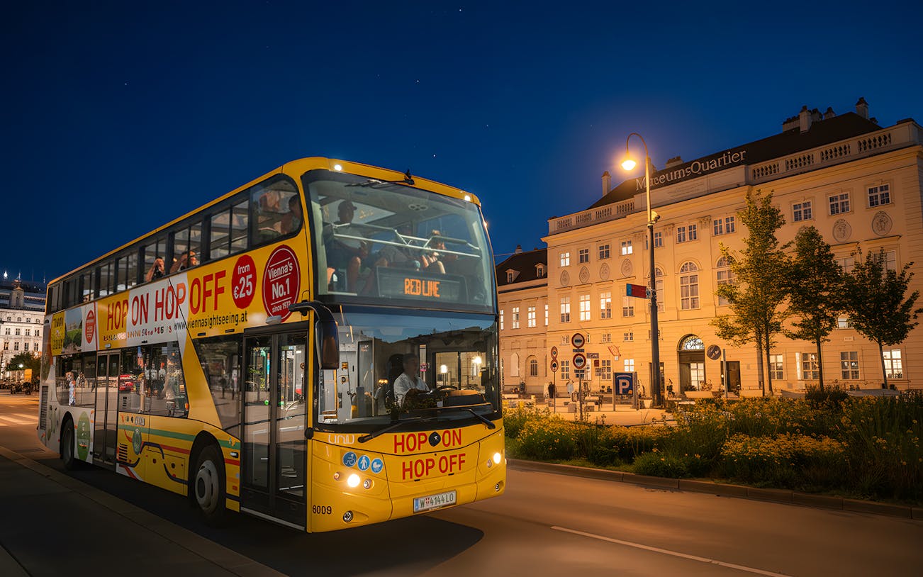 Hop-on hop-off bus in front of MuseumsQuartier, Vienna, during evening sightseeing tour.