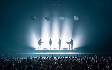 Silhouetted performers on stage with audience at ABBA Voyage show in London.