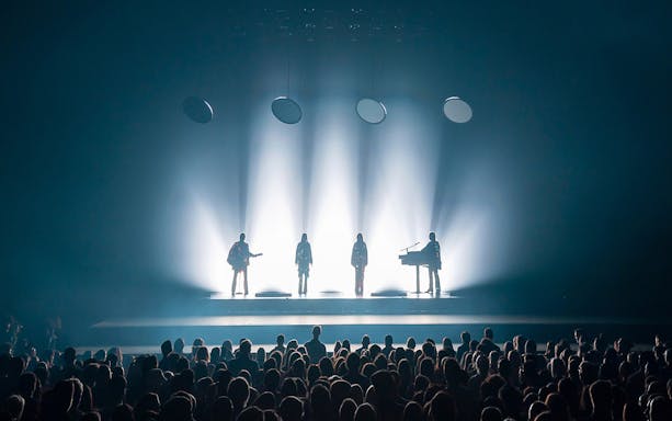 Silhouetted performers on stage with audience at ABBA Voyage show in London.