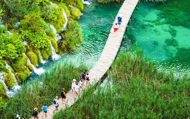 Tourists walking on a wooden path over turquoise water in Plitvice Lakes National Park.