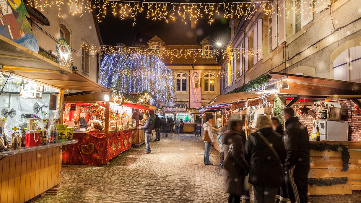 Christmas market in Colmar, France with festive lights and people browsing stalls.