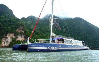 Catamaran Ombre Yacht sailing near lush cliffs in Phuket, Thailand.