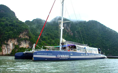 Catamaran Ombre Yacht sailing near lush cliffs in Phuket, Thailand.