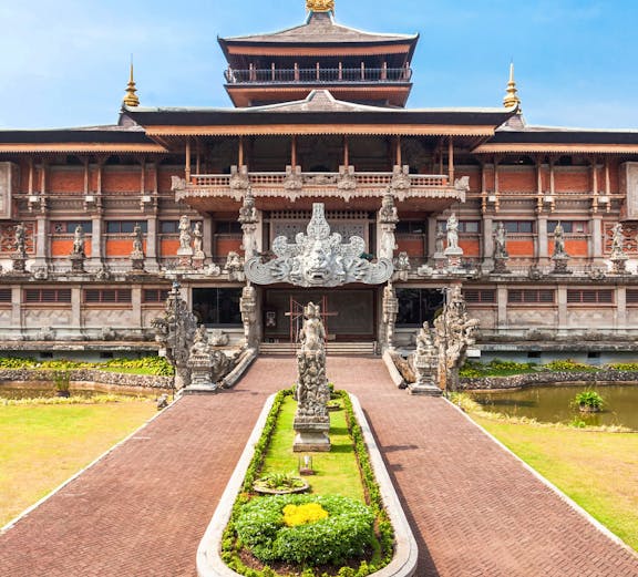 Taman Mini Indonesia traditional building with ornate statues and garden path.
