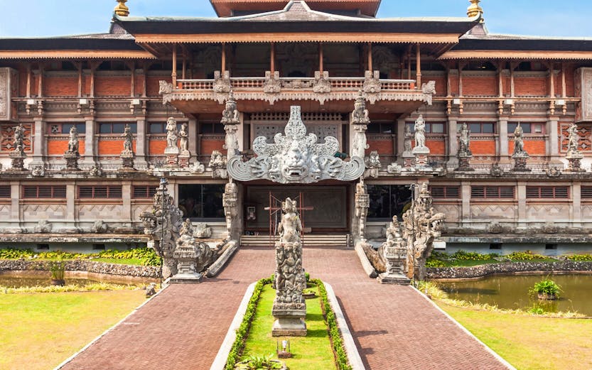 Taman Mini Indonesia traditional building with ornate statues and garden path.