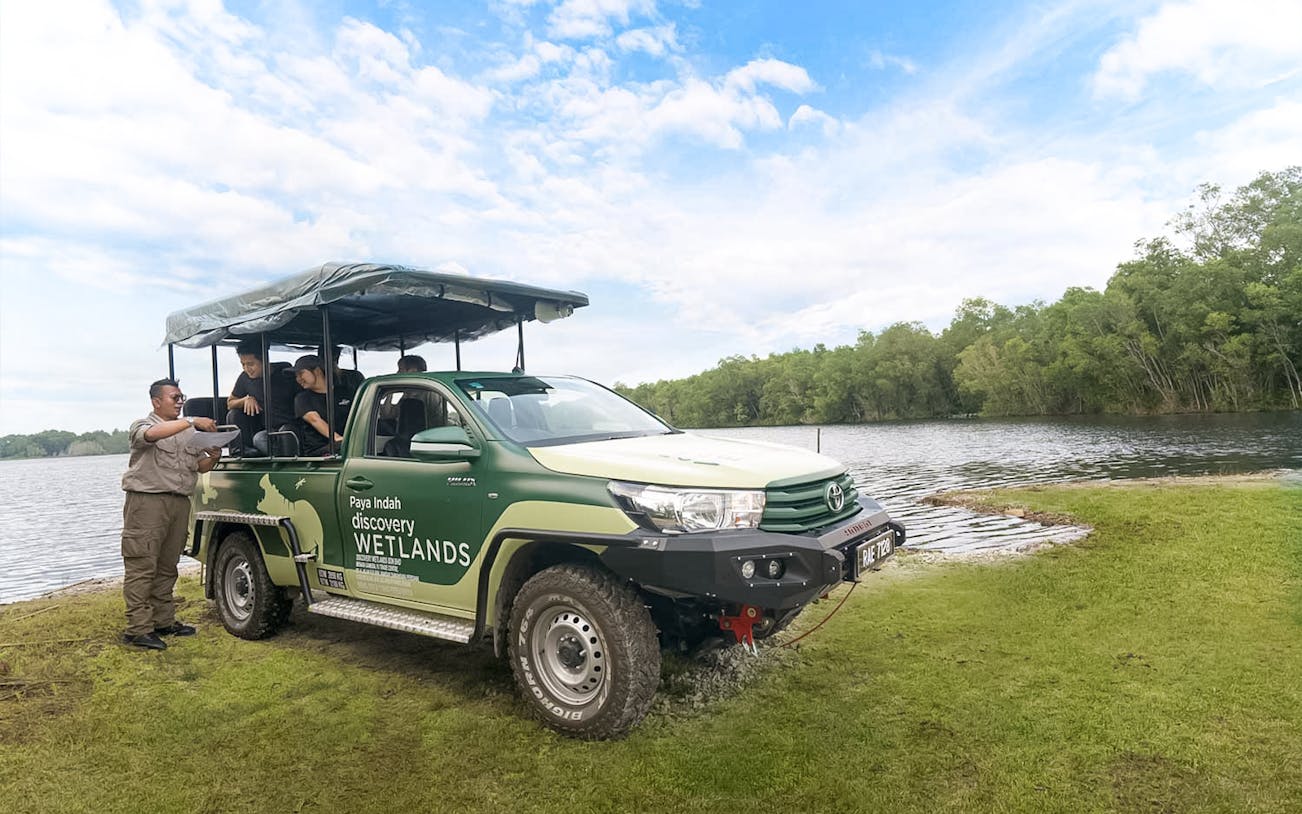 Safari vehicle at Paya Indah Discovery Wetlands, Gamuda Cove, near a lake with tourists.