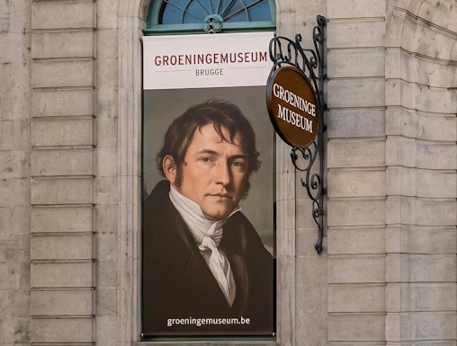 Banner of Groeninge Museum in Brugge with a portrait displayed on a stone building wall.